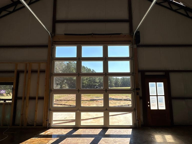 Interior of a garage with large multi-pane glass doors and wooden side door, with rural landscape visible through windows